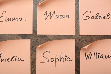 Paper stickers with different names on wooden background, flat lay. Choosing baby's name