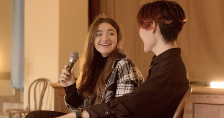 Happy smiling girl speaks into the microphone, laughing cheerfully and expressing positive emotions. Asian guy supports her laughter, creating a lively and jovial atmosphere indoor. Students talking.