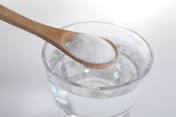 Spoon with baking soda over glass of water on white background, closeup