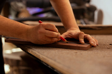 Artisan using ruler to take measurements of plank used to make creative wood sculptures in studio....