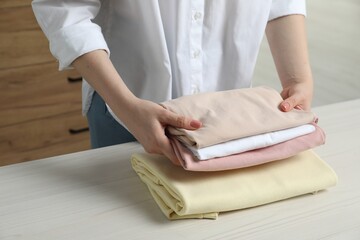 Woman folding clothes at white wooden table indoors, closeup