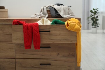 Cluttered chest of drawers indoors. Clothes in mess