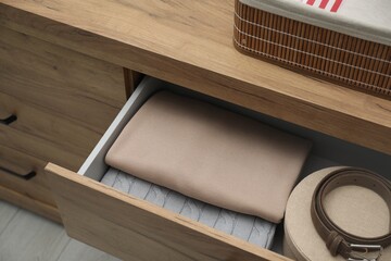 Chest of drawers with different folded clothes and accessories indoors, closeup