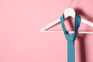 Hanger with turquoise tie on pink background. Space for text