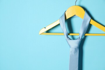 Hanger with silk tie on light blue background. Space for text