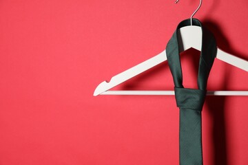 Hanger with black tie on red background. Space for text