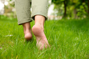 Woman walking barefoot on green grass outdoors, closeup