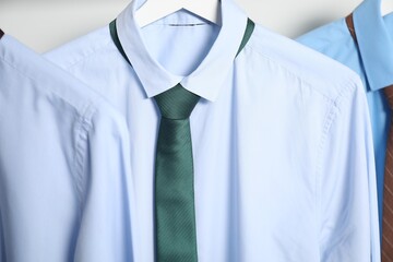Hangers with shirts and neckties on light background, closeup