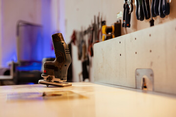 Close up shot of electric router on workbench in assembly shop with woodworking tools on rack in...