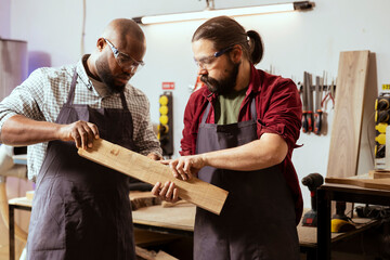 Manufacturer and apprentice wearing safety glasses selecting high quality wood materials. Cabinetmaker and colleague using protective equipment doing quality assurance on lumber piece