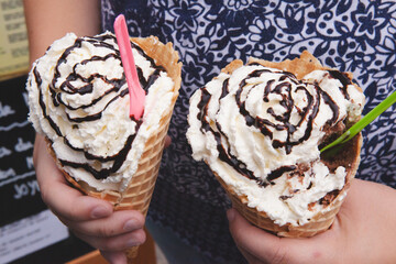 Close up macro shot of a girl holding two ice cream cones with chocolate syrup