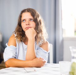 Naklejka premium Upset young girl sitting at the table in her room