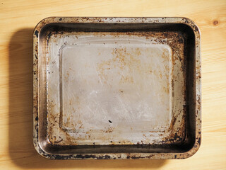 A pan is sitting on a wooden table. The pan is old and has a lot of rust on it. Kitchen hardware...