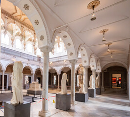 Obraz premium TUNIS, TUNISIA - APRIL 02, 2024: Ornate Carthage Hall in Bardo Museum with elegant Corinthian columns supporting arched gallery framing preserved Roman floor mosaic and statues of gods and emperors