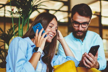 Happy smiling caucasian hipster girl making positive telephone call while spending time with male...