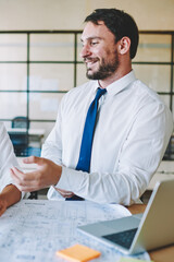 Happy smiling male and female architects discussing ideas for engineering project spending time near desktop with blueprints, successful professionals enjoying working process together with sketches