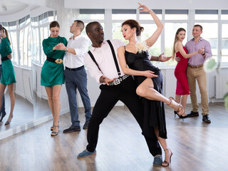 Elegant adult African American performing kizomba paired with attractive woman in red in studio...