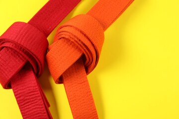 Red and orange karate belts on yellow background, flat lay. Space for text
