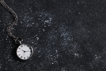Silver pocket clock with chain on dark textured table, top view. Space for text
