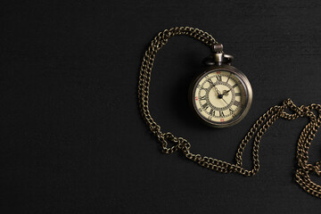 Pocket clock with chain on black wooden table, top view. Space for text