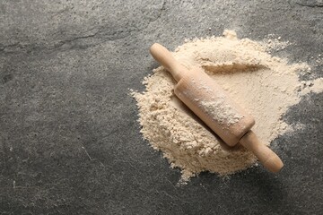 Scattered flour and rolling pin on grey textured table, above view. Space for text