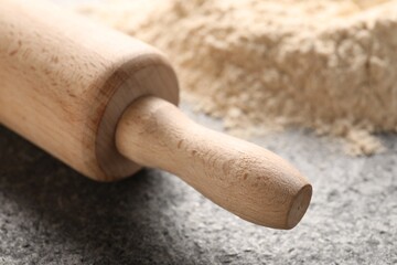 Rolling pin and scattered flour on grey textured table, closeup