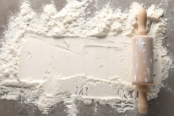 Scattered flour and rolling pin on grey textured table, top view