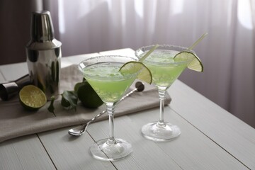 Delicious Margarita cocktail in glasses, limes and bartender equipment on white wooden table