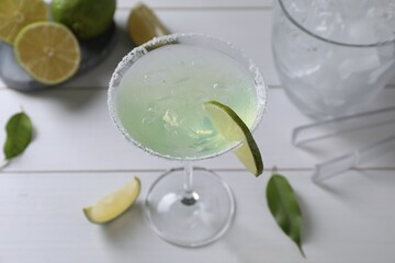 Delicious Margarita cocktail in glass and limes on white wooden table, above view