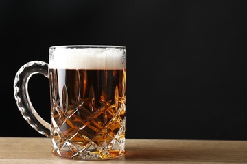 Mug with fresh beer on wooden table against black background. Space for text