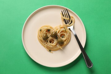 Heart made of tasty spaghetti, fork, olives and cheese on green background, top view