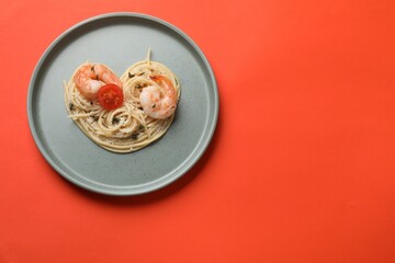 Heart made of tasty spaghetti, tomato, shrimps and cheese on coral background, top view. Space for...