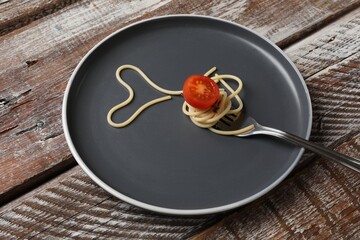 Heart made of tasty spaghetti, fork and tomato on wooden table