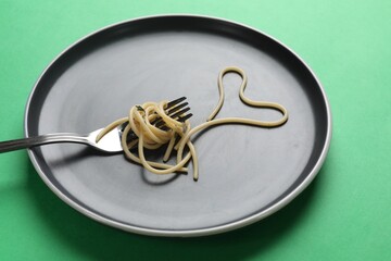 Heart made of tasty spaghetti and fork on green background