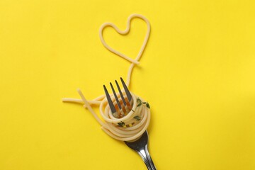 Heart made of tasty spaghetti and fork on yellow background, top view