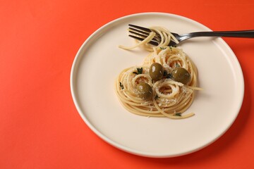 Heart made of tasty spaghetti, fork, olives and cheese on coral background. Space for text
