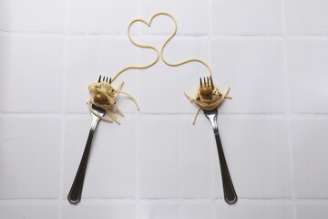 Heart made of tasty spaghetti, forks and olives on white tiled table, top view
