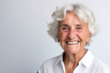 A cheerful senior woman with white hair and a radiant smile wearing a white shirt poses against a plain backdrop - Generative AI