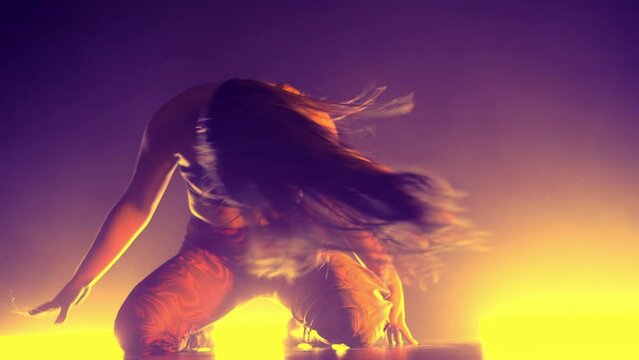 Alluring woman dancing flexible movements with body on floor. Erotic hot dance in dark studio with neon light. Lady dancer in tight clothes and heels.
