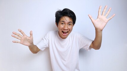 Young Asian man in white shirt with funny expression, excited, laughing with open hand gesture