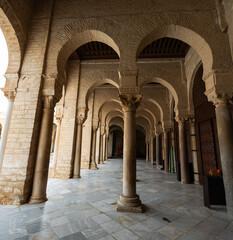 Obraz premium Long corridors under vaulted ceiling in ancient mosque of Kairouan in Tunisia. Colonnade in patio of Islamic temple. Religious Islamic building, place of worship prayer for many generations of Muslims