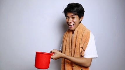 young Asian man wearing a white shirt, towel and holding a ladle to prepare to take a shower with...