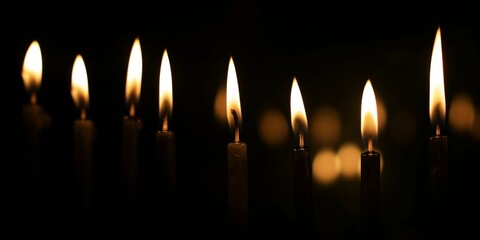 Multiple candles with flames burning brightly against a dark black background
