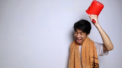 young Asian man wearing a white shirt, towel and holding a ladle to prepare to take a shower with...