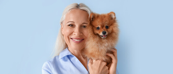 Mature woman with Pomeranian dog on blue background, closeup