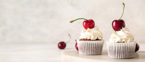 Board with tasty cherry cupcakes on light background