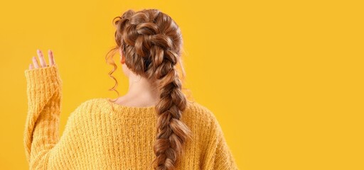 Young woman in warm sweater and with braided hair on yellow background with space for text, back...