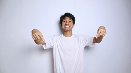 Excited young Asian man in white shirt gestures pointing down