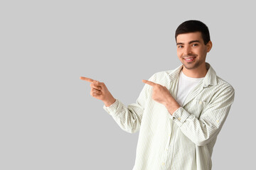 Young man pointing at something on light background