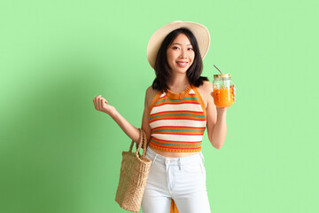Beautiful Asian woman with glass of juice on green background